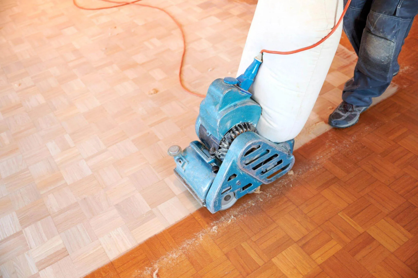 Wood Floor Sanding in Brockley being carried out on an oak parquet floor, with a blue belt sander exposing fresh, lighter timber beside the still‑varnished blocks.