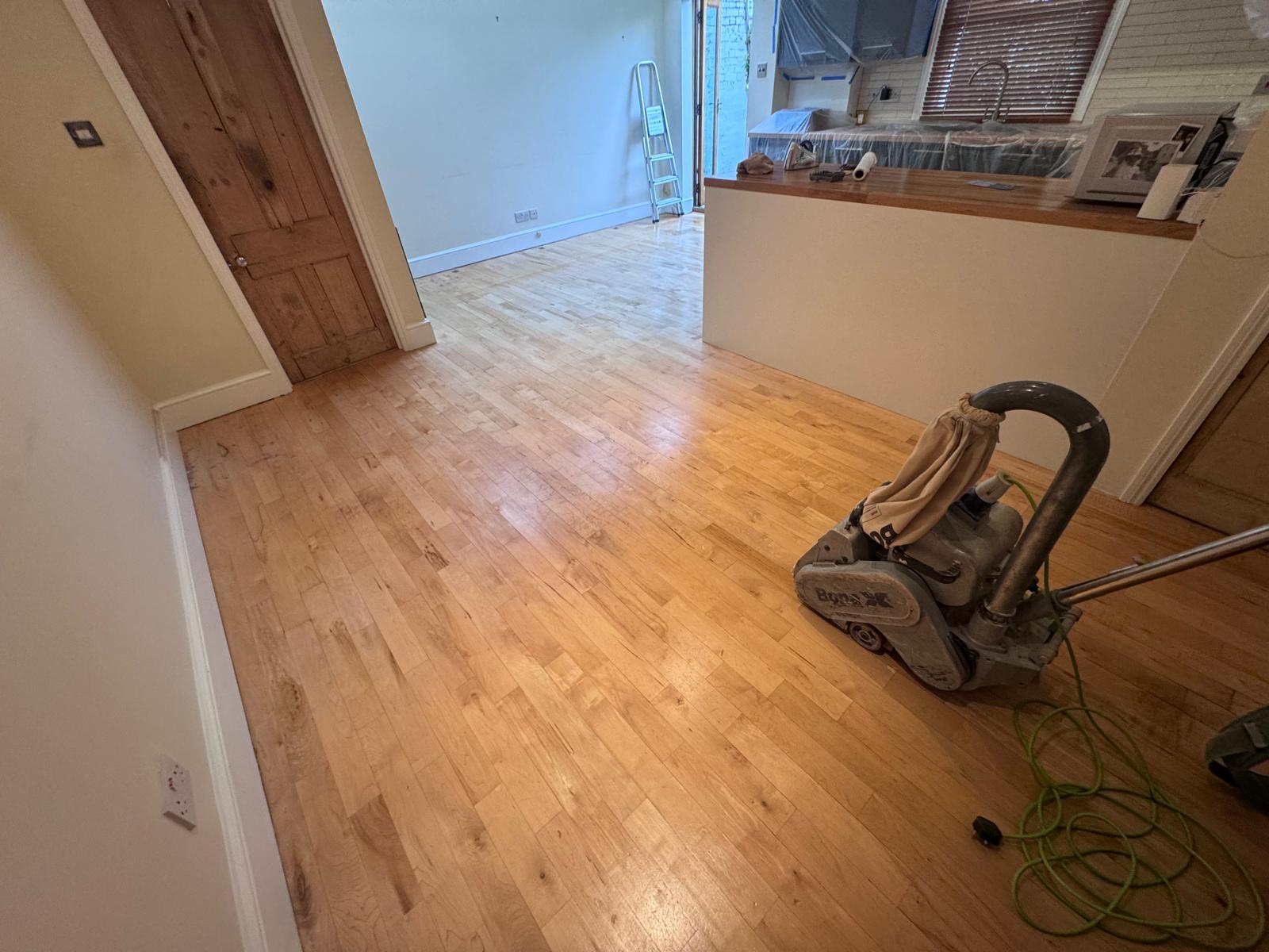 Hardwood Floor Sanding in Brockley – Light Oak Hardwood Strip Floor Restoration Hardwood floor sanding in Brockley on a light oak hardwood strip floor in an open-plan living room, with a professional floor sanding machine in use near the kitchen area.